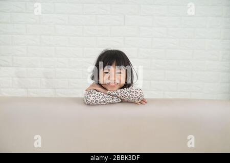 Fröhliche aufgeregt asiatischen jungen Mädchenkopf, der hinter dem Sofa schälte Stockfoto