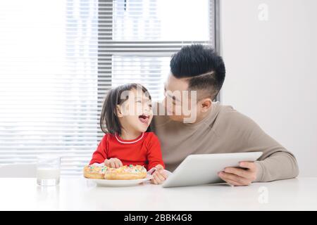 Der junge Vater und seine Tochter essen Pizza und benutzen das ipad. Stockfoto