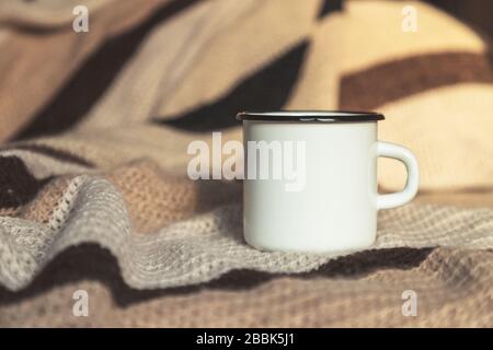 Weißer Lagerfeuer Emaille Kaffeebecher mit handgewebter Decke. Leerer Becher zum gestalten. Stockfoto