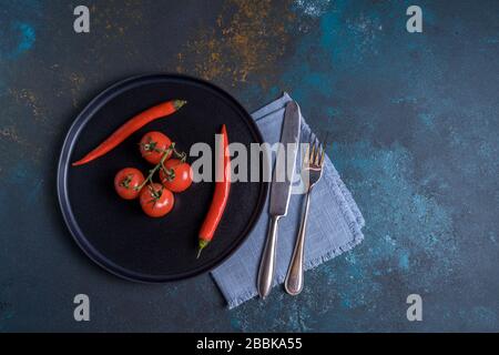 Flach legen Sie einen kleinen Haufen reifer frischer Tomaten und Chilipapripper auf einen schwarzen Teller. Stockfoto