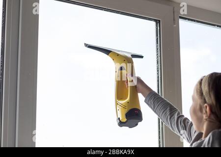 Kleines Mädchen wäscht großes Fenster im Wohnzimmer mit einem tragbaren professionellen Staubsauger. Mädchen wäscht Fenster zu Hause. Kinder helfen zu Hause. Hilfe Stockfoto