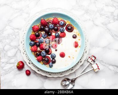 Blaue Schüssel mit warmem Haferbrei, Müsli und Cornflakes mit frischen Beeren, Erdbeeren, Kirschen und Blaubeeren von oben. Stockfoto