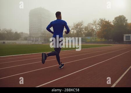 Ein junger Athlet läuft auf ein Stadion im Nebel. Stockfoto