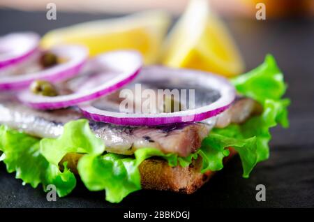 Appetitliches Smorrebrod mit norwegischem Hering, Salat, blauer Zwiebel, Zitrone und Tomate liegt auf einem Holzbrett Stockfoto