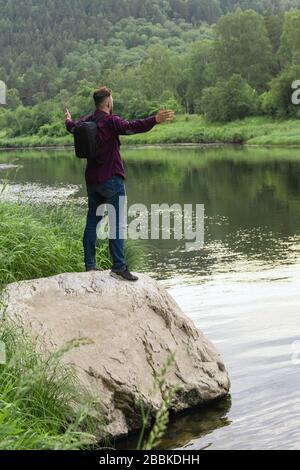 Rückansicht Porträt des jungen Mannes Tourist auf großen Stein auf einem schmalen Waldufer mit Armen geöffnet breit zur Freude stehen. Tourismus, Wandern, aktiv le Stockfoto