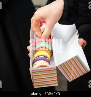 Frau Hand nimmt den Kuchen. Traditionelle französische bunte Makronen in einer Reihe in einer Schachtel. Stockfoto