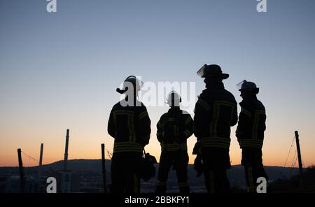 Stuttgart, Deutschland. April 2020. Feuerwehrleute stehen nach einer Operation am Morgen auf einer Wiese. Credit: Sebastian Gollnow / dpa / Alamy Live News Stockfoto