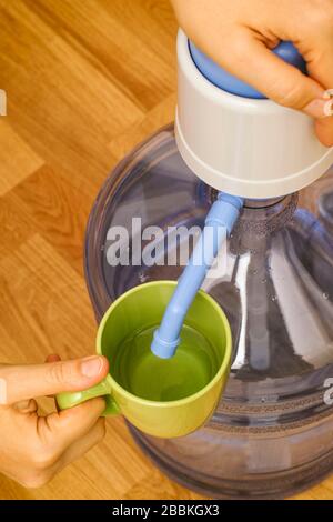 Frau schüttet Wasser in grünem Becher aus der Flasche mit Wasserpumpe. Stockfoto