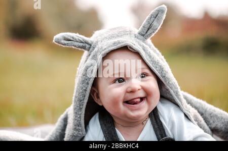 Wunderschönes, süßes, bezauberndes Baby, das draußen auf dem Gras sitzt, lacht und schmilzt, sieht glücklich aus Stockfoto