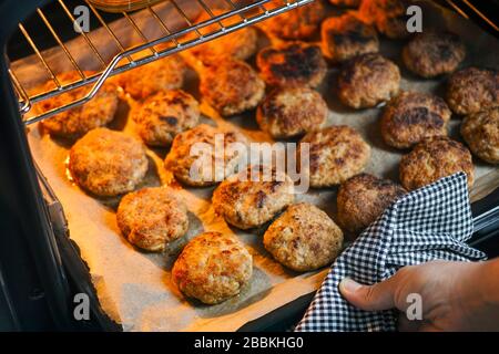 Frau Hand mit Serviette, die Backblech mit Häckchen aus dem Ofen herausnimmt. Nahaufnahme Stockfoto