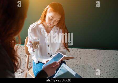 Weibliches Modell liest ein Buch in einem Café. Junge Frau sitzt mit ihrem Freund in einem Restaurant und trinkt Kaffee Stockfoto