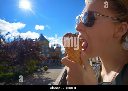 Hübsches Mädchen isst bei heißem Wetter in der Stadt großes Eis. Profilporträt mit selektivem Fokus. Reisen Sie nach Kanada. Stockfoto