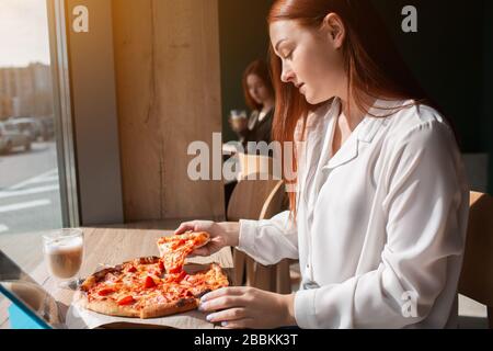 Weibliches Modell hält ein Stück Pizza in den Händen. Junge Frau, die Pizza isst. Stockfoto