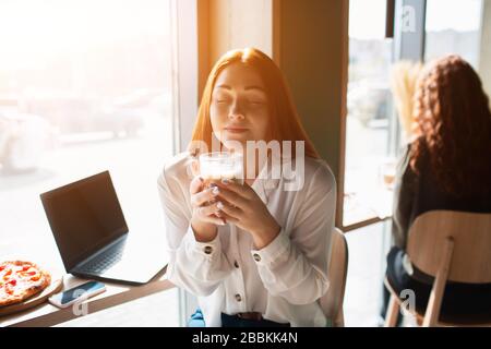 Junge Frau hält eine Tasse Kaffee in der Hand. Weibliches Modell hält einen Becher mit geschlossenen Augen Stockfoto