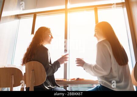 Weibliche Models sitzen und sprechen im Café. Junge Frauen, die während des Mittags Kaffee trinken Stockfoto