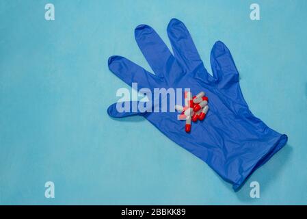 Rote und weiße Pillen liegen auf einem blauen medizinischen Handschuh Stockfoto