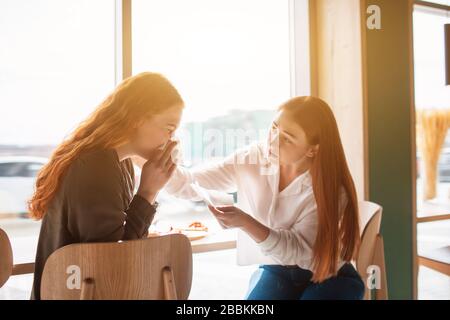 Weibliches Modell sitzt mit ihrem Freund in einem Café und bläst ihre Nase. Junge Frau ist krank. Stockfoto