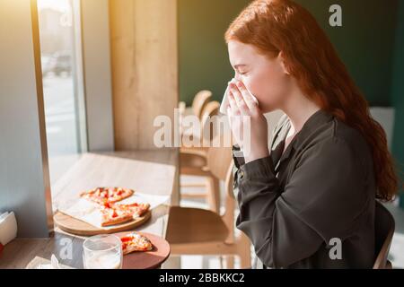 Junge Frau bläst ihre Nase in einer Serviette. Weibliches Modell sitzt an einem Tisch und wischt ihre Nase Stockfoto