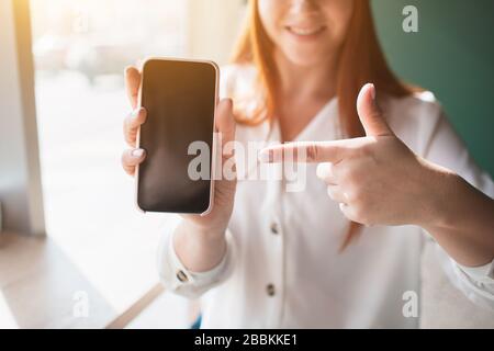 Zeigefinger zeigt auf Nahaufnahme des Telefons. Junge Frau hält und benutzt ein Smartphone in ihren Händen. Stockfoto