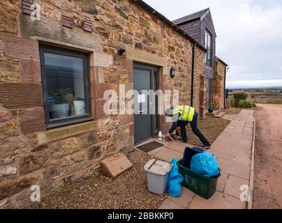 East Lothian, Schottland, Großbritannien. April 2020. Lokale Lebensmittellieferungen während der Pandemie von Covid-19 Coronavirus: Die Molkereien der Yester Farm beginnen zweimal wöchentlich mit kostenlosen Hauslieferungen an Einwohner in East Lothian. Yester Mains ist ein Familienbetrieb, der preisgekrönte Molkereiprodukte für Handwerker liefert. Sie wurden mit Aufträgen überflutet. Abgebildet: Dale, der normalerweise Käse in der Molkerei herstellt, bringt Milch und Joghurt zu Hause an eine Familie, die sich selbst isoliert Stockfoto