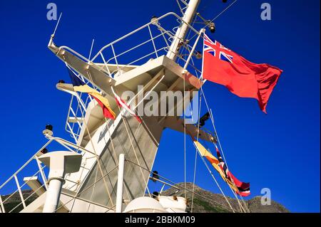 Flaggen fliegen auf dem Mast eines britischen Kreuzfahrtschiffs in den norwegischen Fjorden. Bunte Schilder und Navigationsgeräte, die sich gegen einen blauen Himmel abschimmern Stockfoto