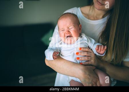 Porträt eines Neugeborenen. Mutter hält ein Kind in den Armen. Ein Neugeborenes schreit. Magenschmerzen, Krämpfe im Kindesalter. Weinendes Neugeborenes. Die erste Stockfoto