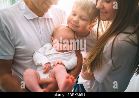 Mutter und Vater halten ein Baby in den Armen. Der große Bruder umarmt seine Schwester. Pflege und Gesundheit. Frohe junge Familie Stockfoto