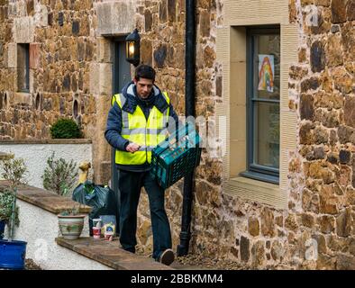 East Lothian, Schottland, Großbritannien, 1. April 2020. Lokale Lebensmittellieferungen während der Pandemie von Covid-19 Coronavirus: Die Molkereien der Yester Farm beginnen zweimal wöchentlich mit kostenlosen Hauslieferungen an Einwohner in East Lothian. Yester Mains ist ein Familienbetrieb, der preisgekrönte Molkereiprodukte für Handwerker liefert. Sie wurden mit Aufträgen überflutet. Dargestellt: Dale, der normalerweise Käse in der Molkerei herstellt, bringt die ersten Hauslieferungen von Milch zu einem ländlichen Stechen mit einem Regenbogen der Hoffnung in das Fenster Stockfoto