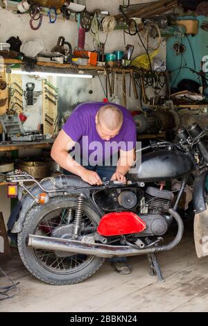 Mann repariert altes Motorrad in der Garage, vor dem Hintergrund der Werkzeuge Stockfoto