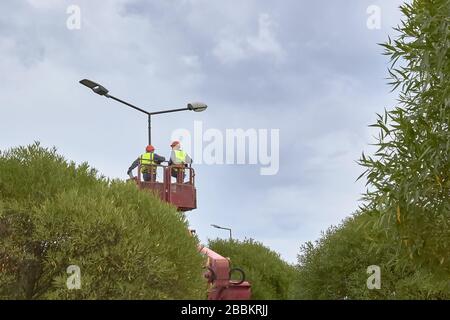 Sankt Petersburg, RUSSLAND - 11. Juli 2019: Arbeiter im Hubeimer reparieren Straßenlichtholzstange mit Doppelkopf und ändern die Beleuchtung auf Diode. Stockfoto