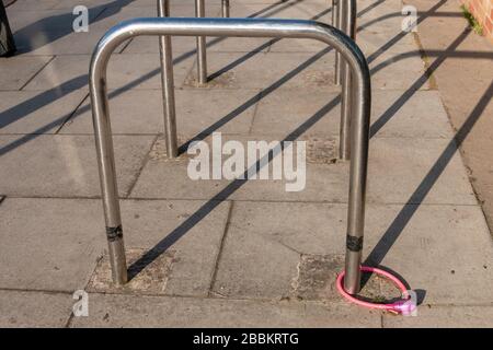 Nahansicht eines rosafarbenen Fahrradschlosses und einer Kette, die mit einem Metall-Fahrradpfosten verbunden sind Stockfoto