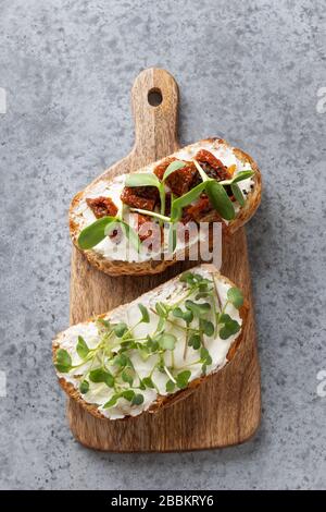 Sandwiches auf Toast mit verschiedenen Tomaten, frischen Radie-Mikrogrüns, Frischkäse auf grauem Hintergrund. Draufsicht. Vertikales Format. Stockfoto