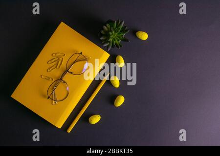 Gelber Bleistift, gelbe Notizbuchgläser, Stifte, Clippapier und gelbe ostereier auf schwarzem Hintergrund Stockfoto