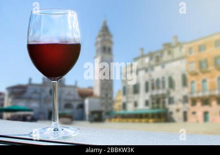 Ein Glas Rotwein auf dem Tisch und italienischer Platz in Venedig mit Turm und bunten Gebäuden, Italien Stockfoto