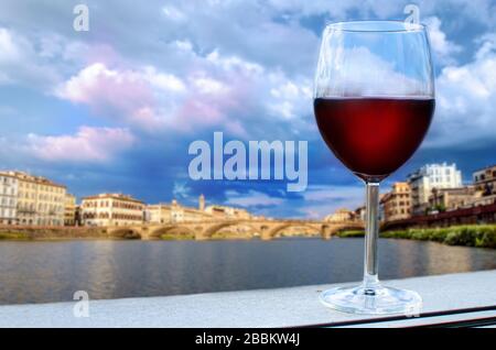 Ein Glas Rotwein mit Blick auf die Brücke in Florenz bei Sonnenuntergang - Ponte alla Carraia, fünfbogenige Brücke über den Fluss Arno in der Toskana Stockfoto