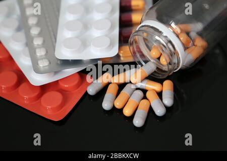Pillen auf einem dunklen Glastisch, Medikamente in Tabletten und Kapseln, die aus einer Flasche verstreut sind. Konzept des Schutzes von Coronavirus, Apotheke, Antibiotika Stockfoto