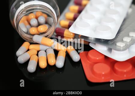 Pillen auf einem dunklen Glastisch, Medikamente in Tabletten und Kapseln, die aus einer Flasche verstreut sind. Konzept des Schutzes von Coronavirus, Apotheke, Antibiotika Stockfoto