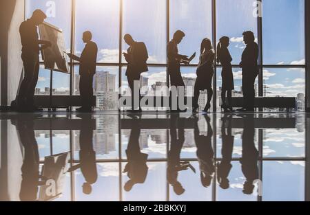 Silhouetten von Menschen gegen das Fenster. Ein Team junger Geschäftsleute, die in einem Büro zusammenarbeiten und miteinander kommunizieren. Unternehmens-Business und Stockfoto