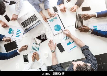 Dokumente, Gadgets und Hände von Personen auf dem Desktop, Draufsicht. Ein Team junger Geschäftsleute, die in einem Büro zusammenarbeiten und miteinander kommunizieren Stockfoto