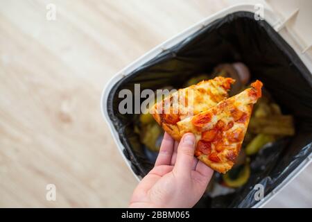 Verschwenden Sie keine Lebensmittel mehr, geben Sie der Frau etwas Essen, Pizza in die Mülltonne, Müll, Essenskonzept Stockfoto