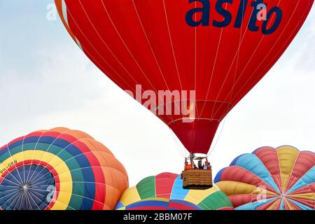 Roter Heißluftballon mit Korb und Menschen, die während des 34. Friese Ballonfeesten Festivals in Joure, Niederlande, über bunten Ballons steigen. Stockfoto