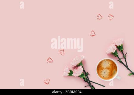 Morgenbecher mit Kaffee und Blumen mit Herzen auf pinkfarbenem Hintergrund. Stockfoto