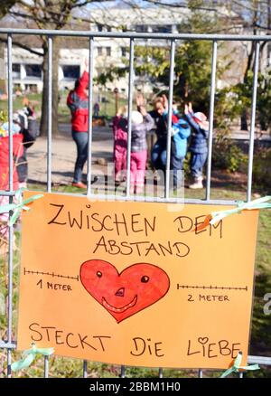 Leipzig, Deutschland. März 2020. In der Kindertagesstätte "Fuchsbau" des DRK-Kreisverbandes Leipzig spielen Kinder mit ihren Lehrern hinter einem Zaun, an dem von Kindern gemalte Bilder angebracht sind. Die Kindertagesstätte ist eine der vielen Einrichtungen, die für die Notfallversorgung von Kindern sorgen, deren Eltern in systemwichtigen Berufen von sechs bis fünf Uhr beschäftigt sind. Kredit: Waltraud Grubitzsch / dpa-Zentralbild / ZB / dpa / Alamy Live News Stockfoto