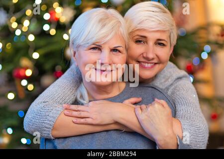 Mutter und Tochter umarmt Weihnachtsbaum Stockfoto