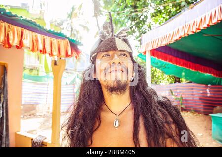 Outdoor-Porträt des jungen amerikanischen Mannes mit langen schwarzen Haaren und indischer Kopfbesinnen Stockfoto