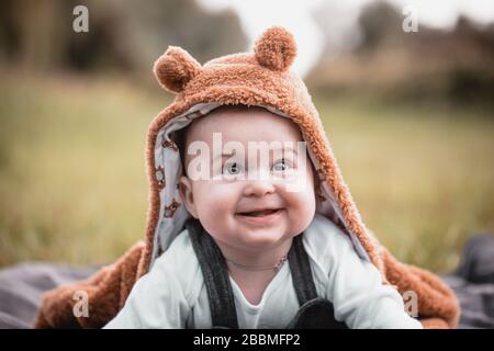 Wunderschönes, süßes, bezauberndes Baby, das draußen auf dem Gras sitzt, lacht und schmilzt, sieht glücklich aus Stockfoto