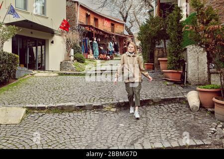 Eine junge kaukasische Frau auf einer Tour durch Istanbul geht eine einsame Straße hinunter. Ein weißes Weibchen, bekleidet in warmer Winterkleidung, spaziert um den Touristenar Stockfoto