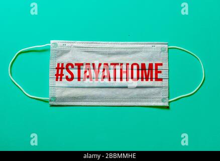 COVID-19, #STAYATHOME. Chirurgische Maske mit Anzeige der Meldung '#ZU HAUSE BLEIBEN', Virus-Prävention und globales Quarantänekonzept auf türkisfarbenem Backgoru Stockfoto