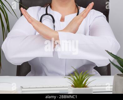 Weibliche Sanitäter sitzen in einem braunen Lederstuhl im Büro und kreuzten ihre Arme vor der Brust, Denial-of-Denial-of-No-Konzept Stockfoto