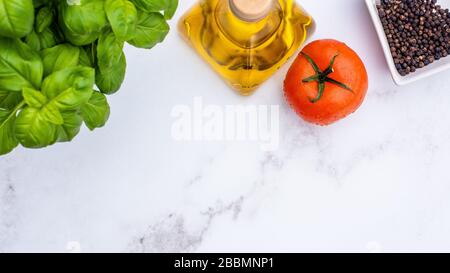 Olivenöl, Tomaten, Basilikum und schwarze Pfeffermais auf einem Arbeitsfläche aus weißem Marmor Stockfoto